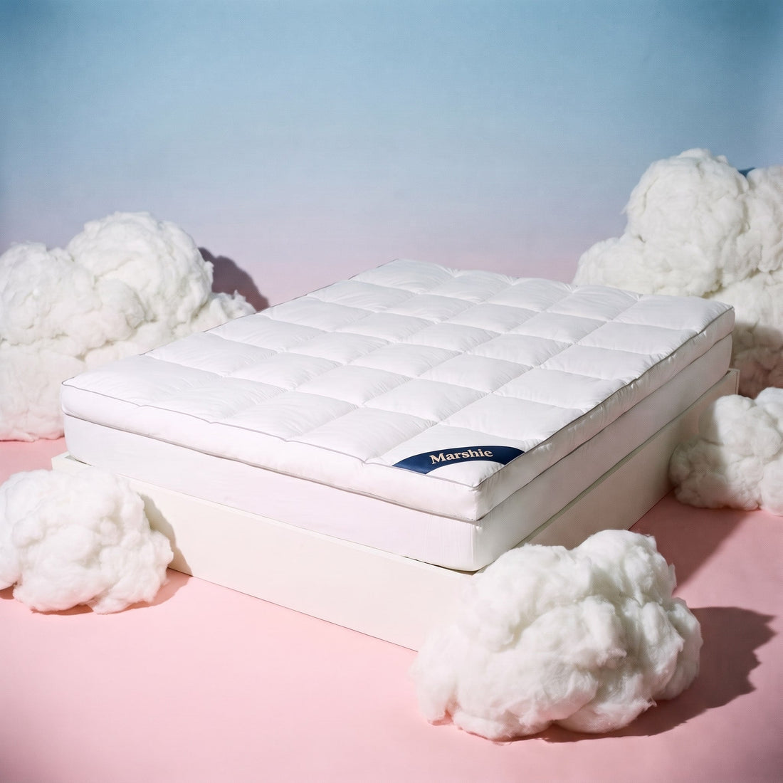 The Marshie Topper on a white bed base surrounded by soft white clouds on a pink and blue set