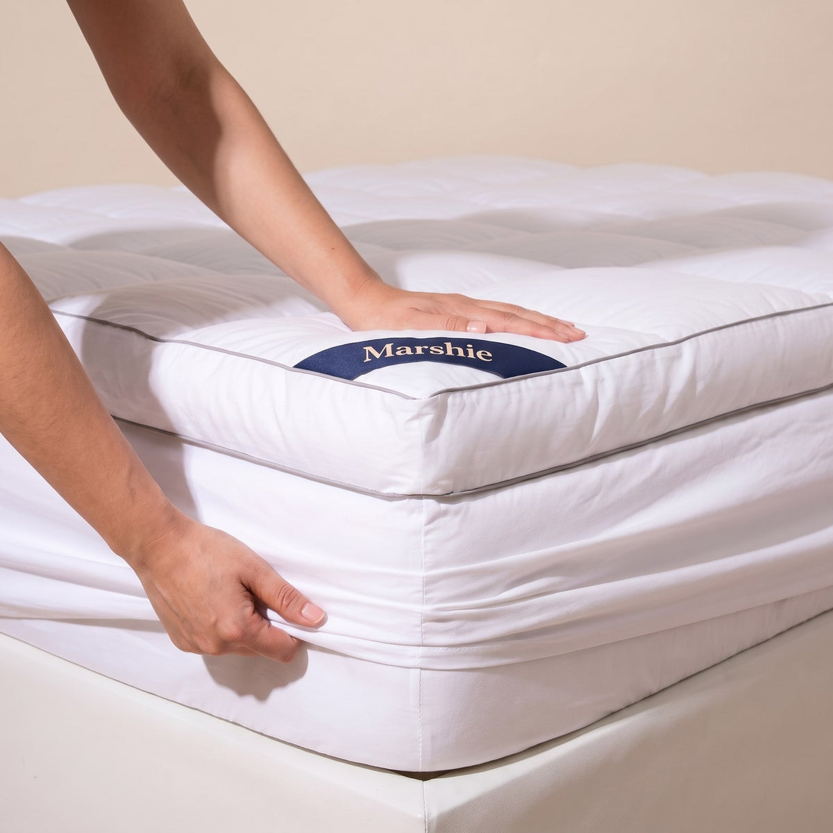 Hands pulling the deep skirt of the Marshie Topper over a mattress